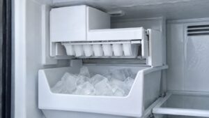 An ice maker module inside a freezer compartment with a partly filled ice bin below it
