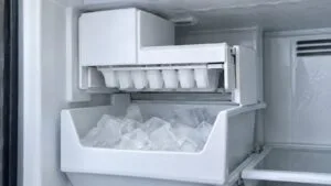 An ice maker module inside a freezer compartment with a partly filled ice bin below it