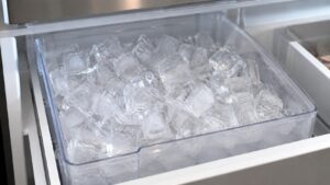 A close-up of a full ice bin with clear, evenly shaped ice cubes inside a built-in refrigerator freezer drawer