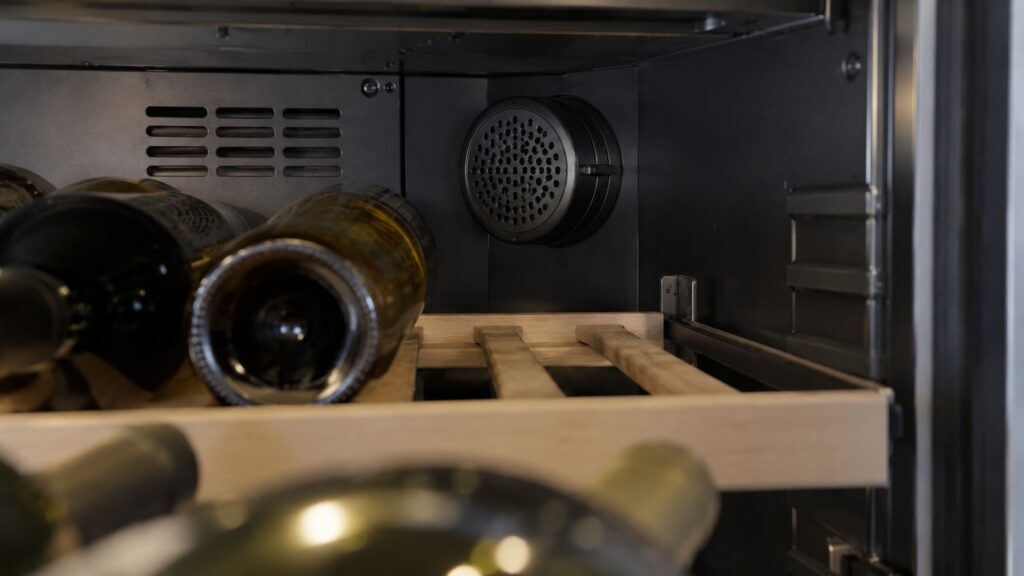 A close-up of a wine cabinet shelf beside the housing of an activated carbon filter at the back
