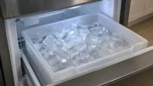 A bin full of clear ice cubes inside an open freezer drawer