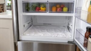 A refrigerator with the lower drawer removed and a towel spread on the floor of the compartment